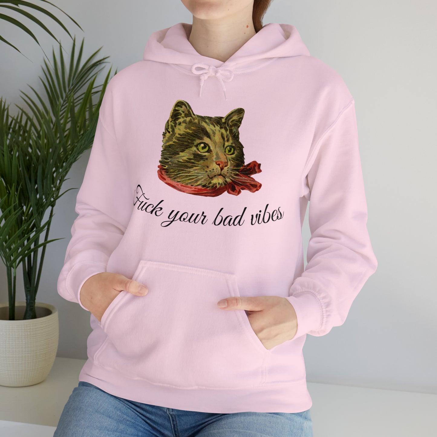 woman wearing light pink hoodie featuring the phrase "Fuck Your Bad Vibes" in elegant cursive beneath a charming vintage graphic of a stylish cat sporting a scarf