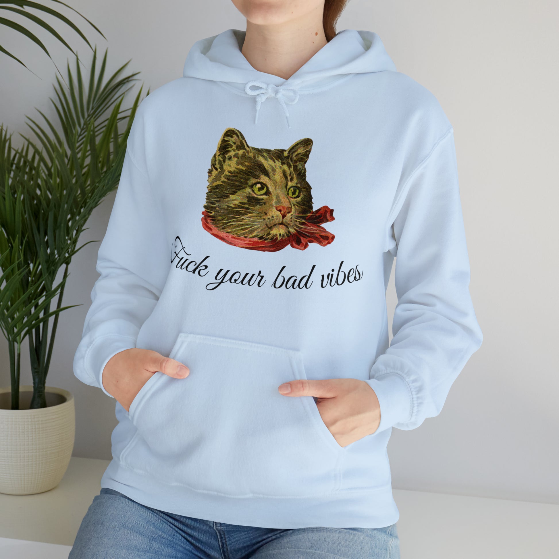 woman wearing light blue hoodie featuring the phrase "Fuck Your Bad Vibes" in elegant cursive beneath a charming vintage graphic of a stylish cat sporting a scarf