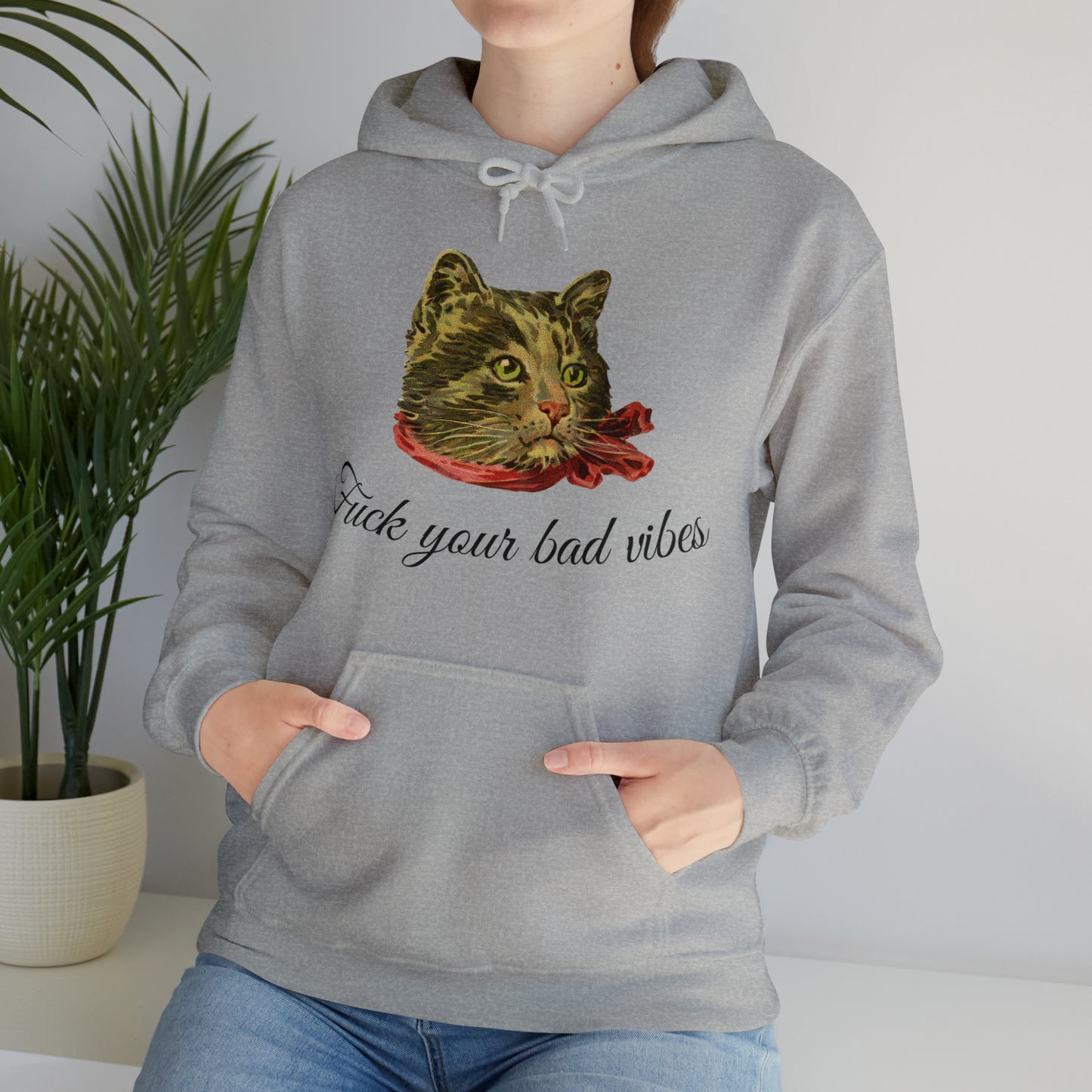 woman wearing light gray hoodie featuring the phrase "Fuck Your Bad Vibes" in elegant cursive beneath a charming vintage graphic of a stylish cat sporting a scarf