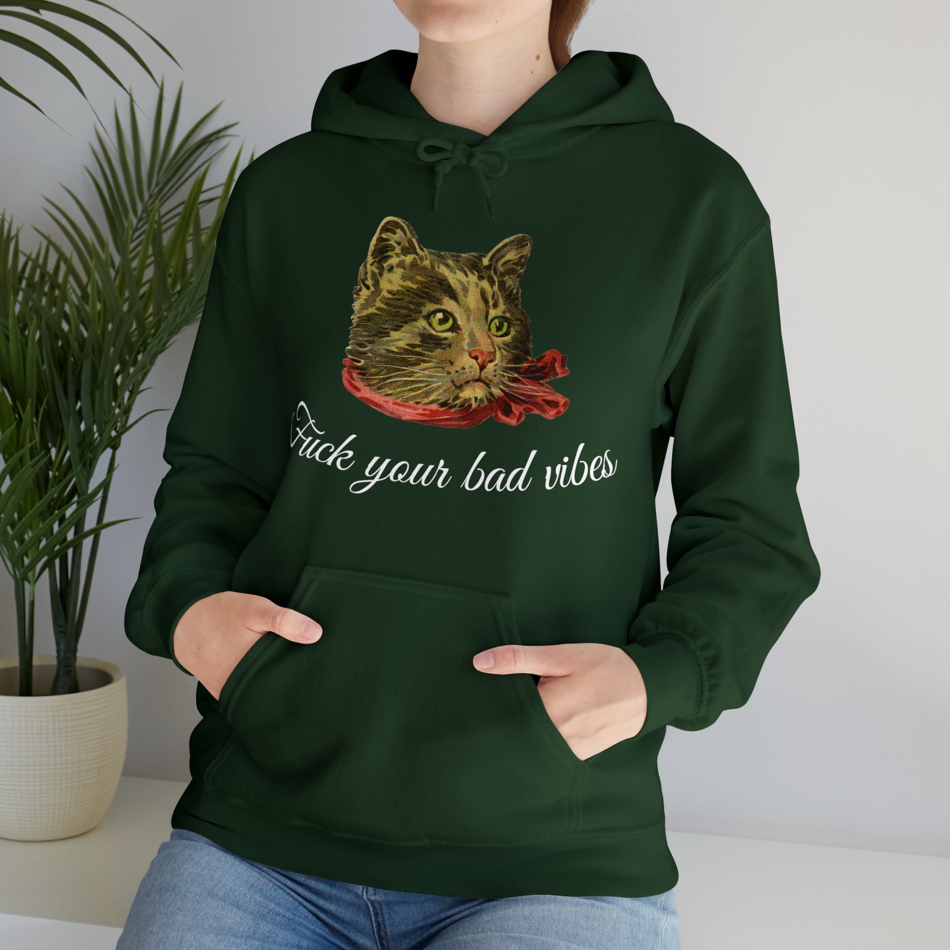 woman wearing forest green hoodie featuring the phrase "Fuck Your Bad Vibes" in elegant cursive beneath a charming vintage graphic of a stylish cat sporting a scarf